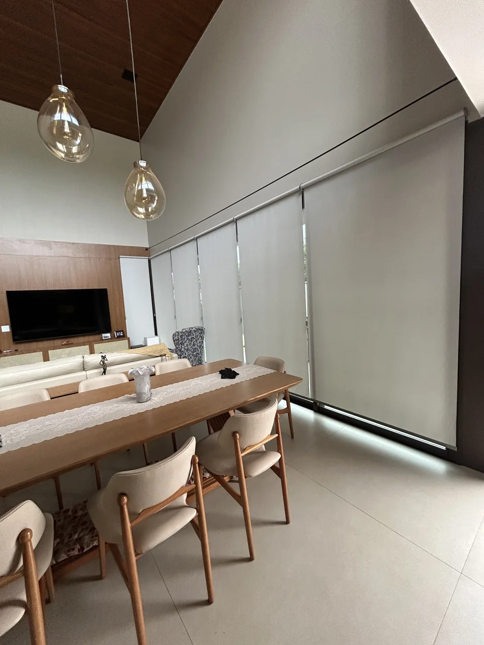 Ambiente gourmet com mesa de jantar, pendentes e persianas rolô nas portas de vidro