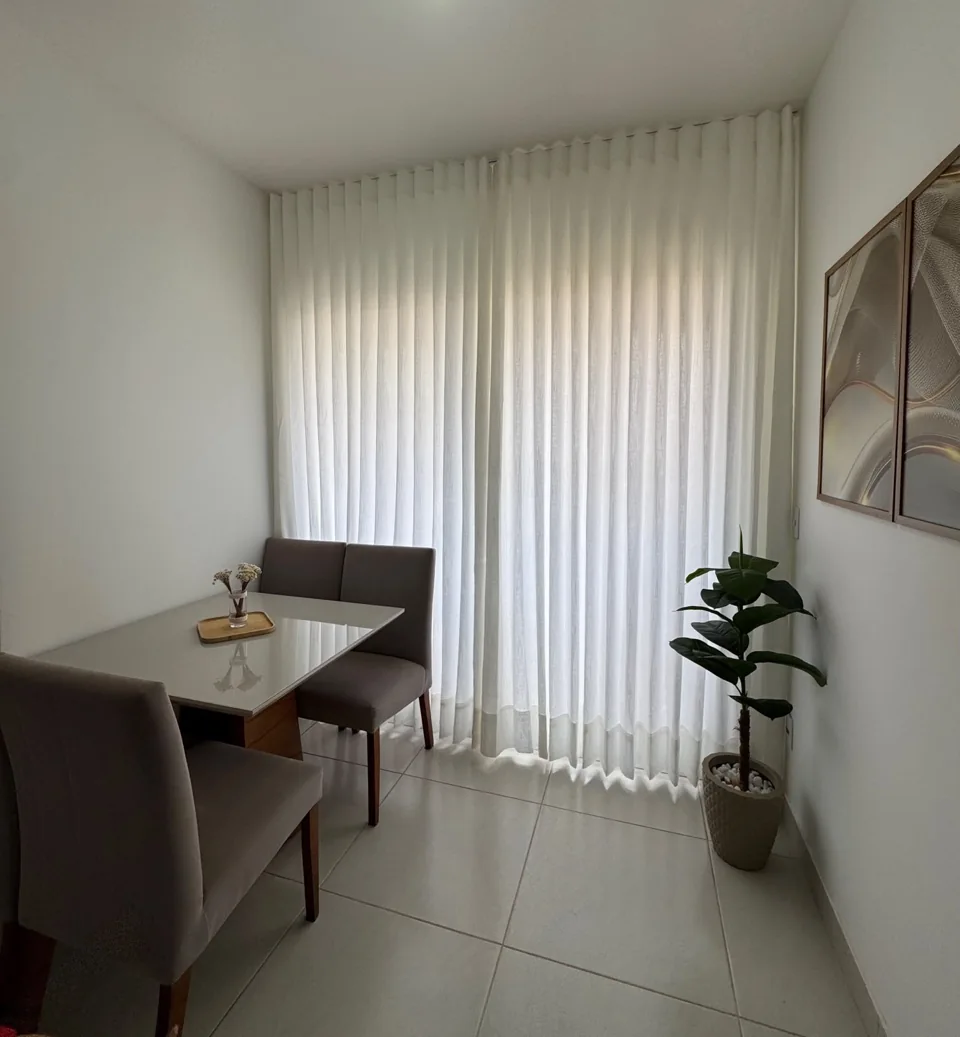 Sala de jantar com cortina branca leve, mesa de vidro e planta junto à janela