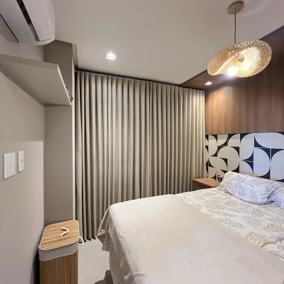 Quarto com cortina bege fechada, cama e cabeceira com painel de madeira