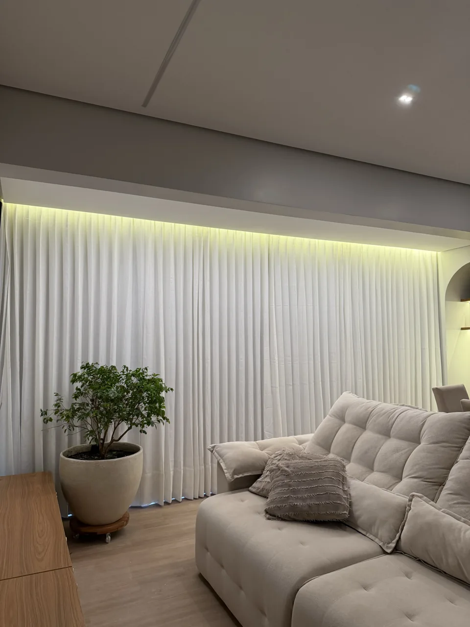 Cortinas claras do teto ao piso em sala com sofá bege e iluminação no cortineiro